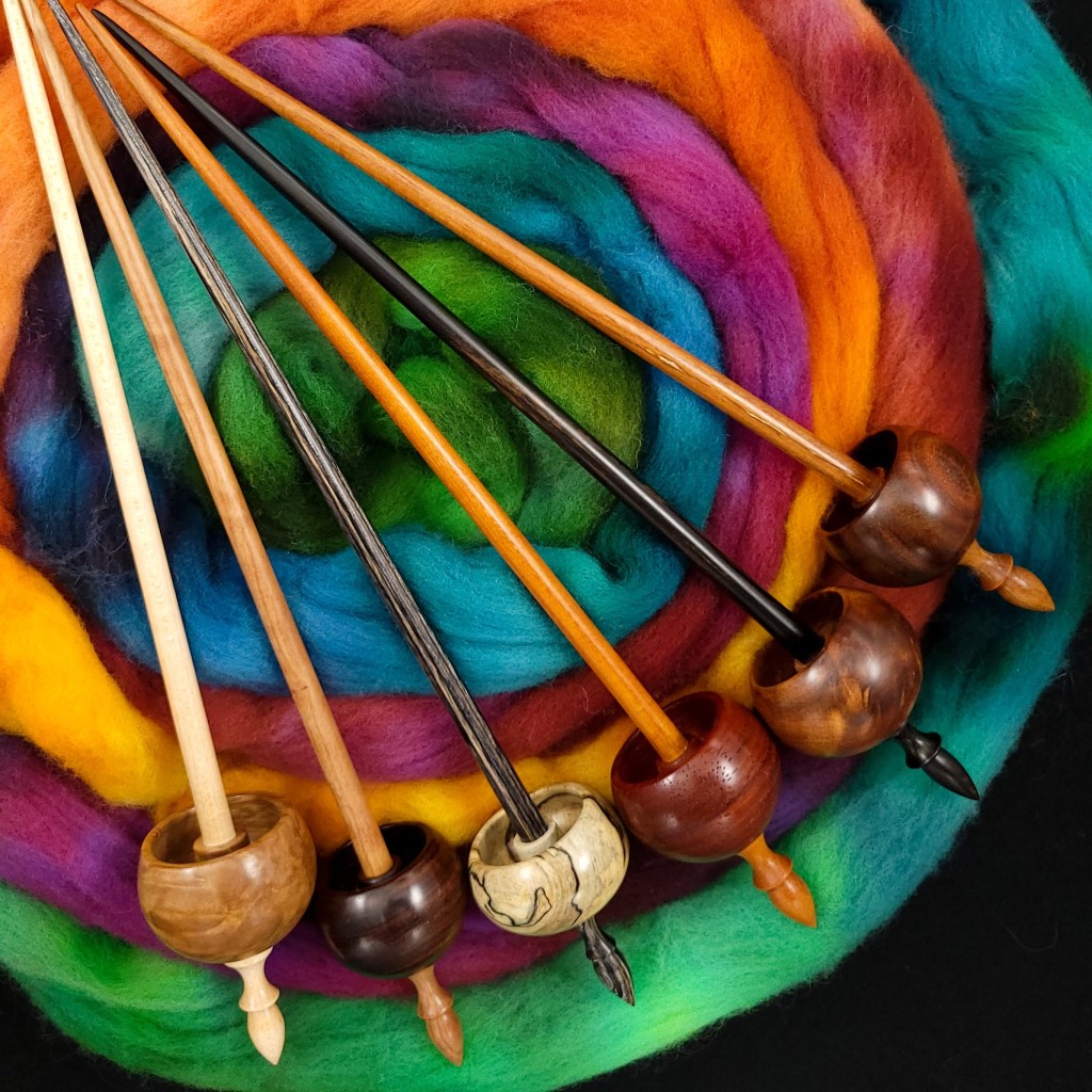 Six Spanish Peaock ninja spindles arrayed on four ounces of rainbow colored targhee 