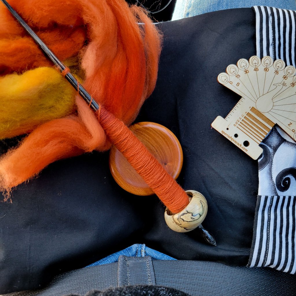 The Spanish Peacock ninja spindle known as "FNG" sitting in a lap with the bowl and a spinning cloth