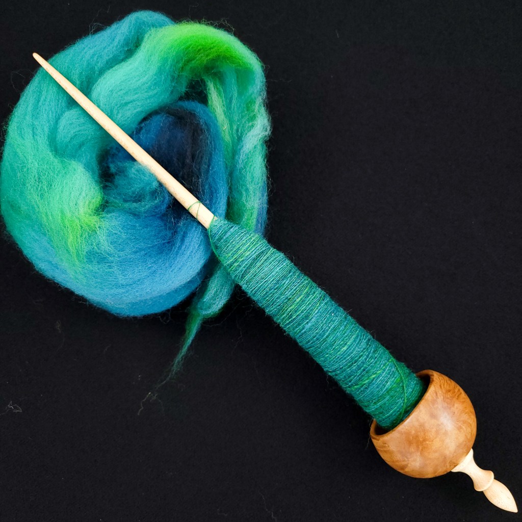 A ninja Spanish Peacock spindle with blue spun fiber 