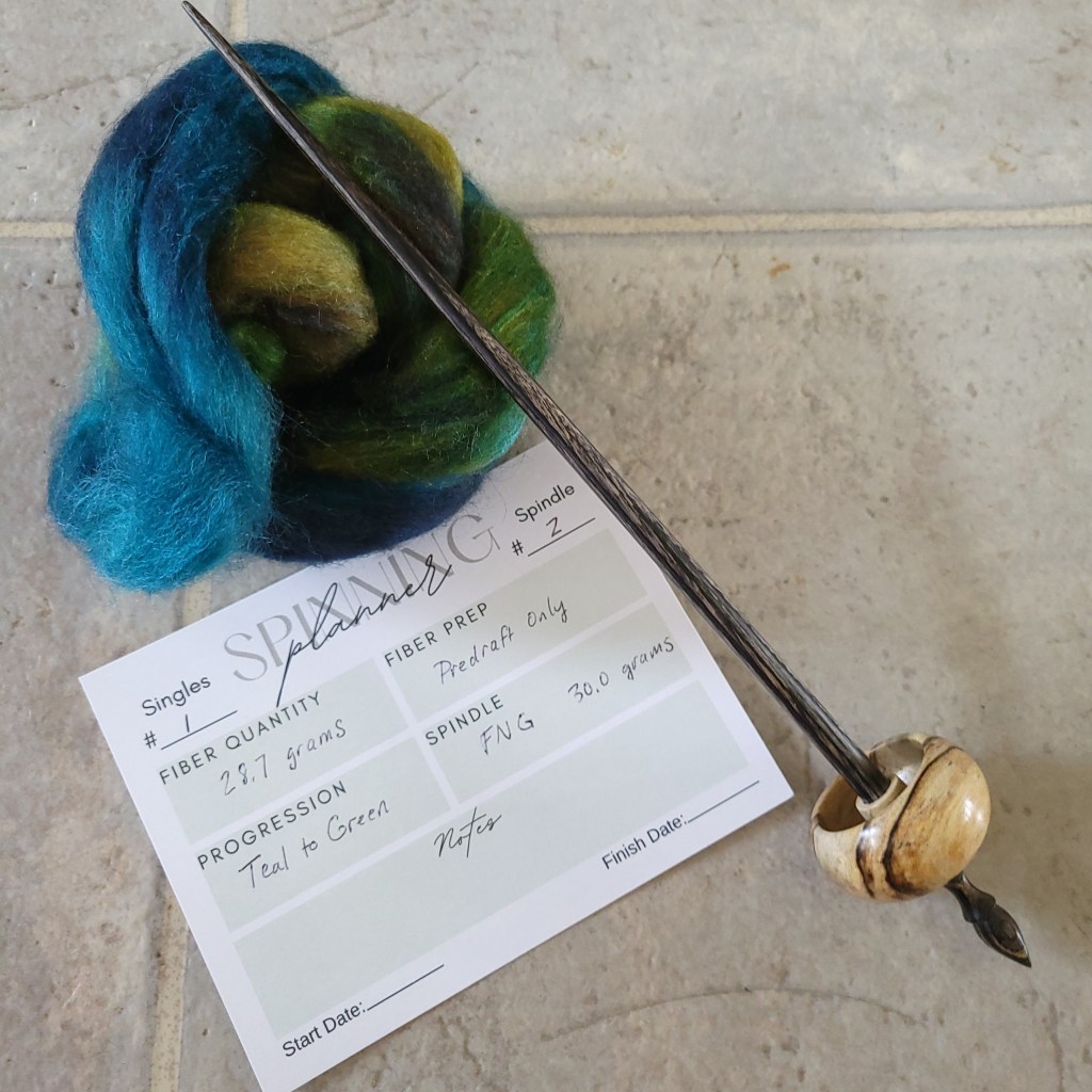 A ball of fiber, a ninja supported spindle, and spinning planner card showing the plan for the spin