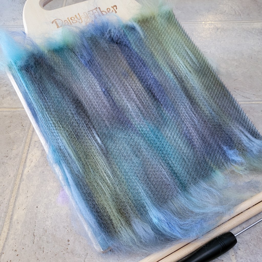 A blending board on a linoleum floor with blue fiber ready to make into rolags for spinning.
