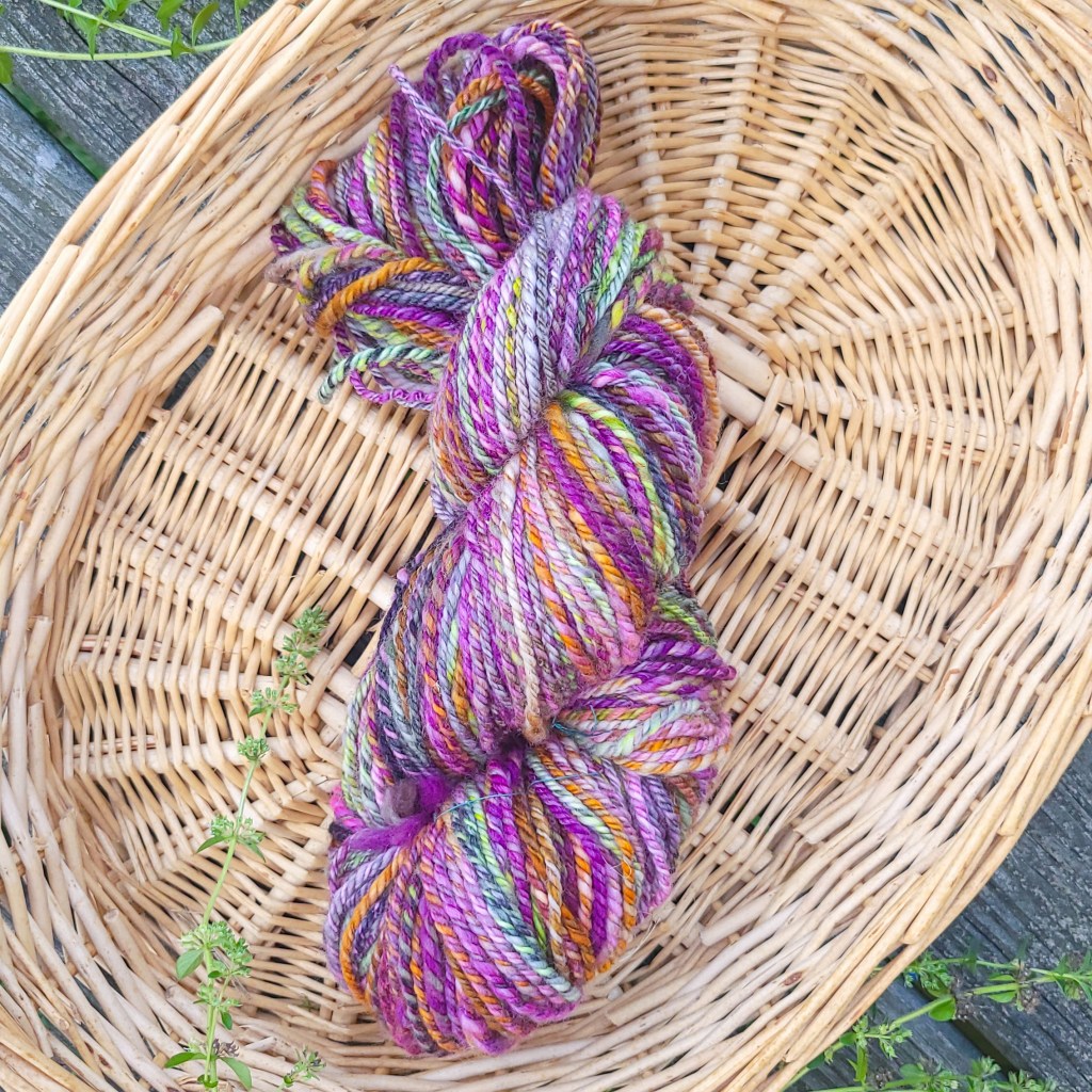 A squishy skein of yarn of multicolored chain ply yarn sits inside a basket