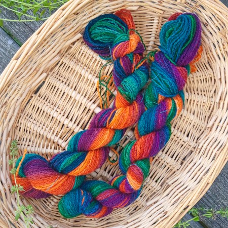 Two skeins of gradient yarn, yellow, orange, blue and green, rest in a basket