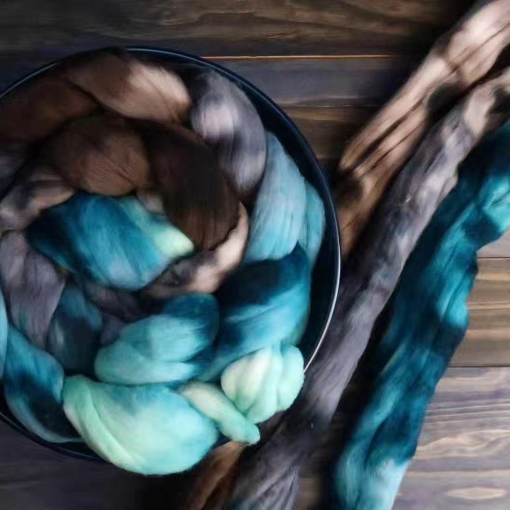 A mint, blue, gray and brown braid lies curled up in a bowl along side the same colored fiber stretched out on a wood background.