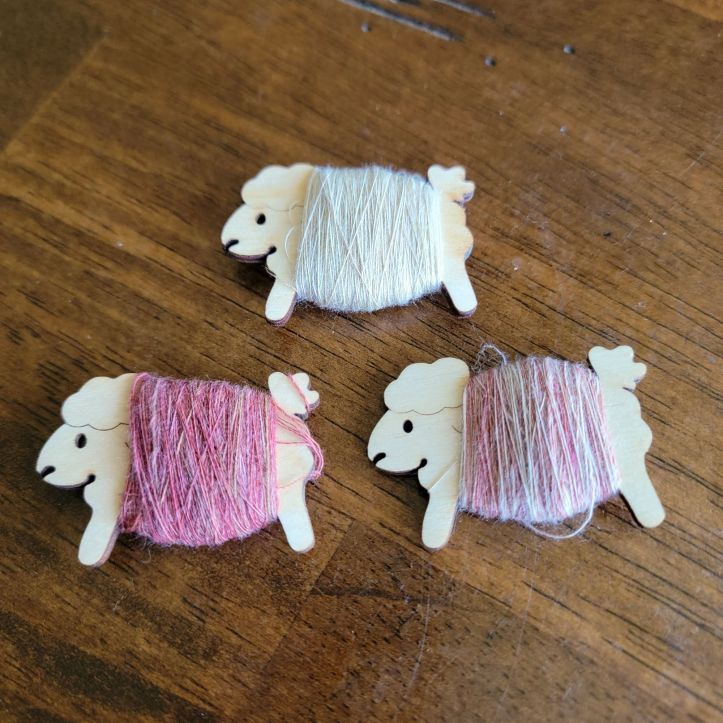 Three sheep-shaped plywood bobbins hold white and pink yarn that had been removed from the wheel bobbins.