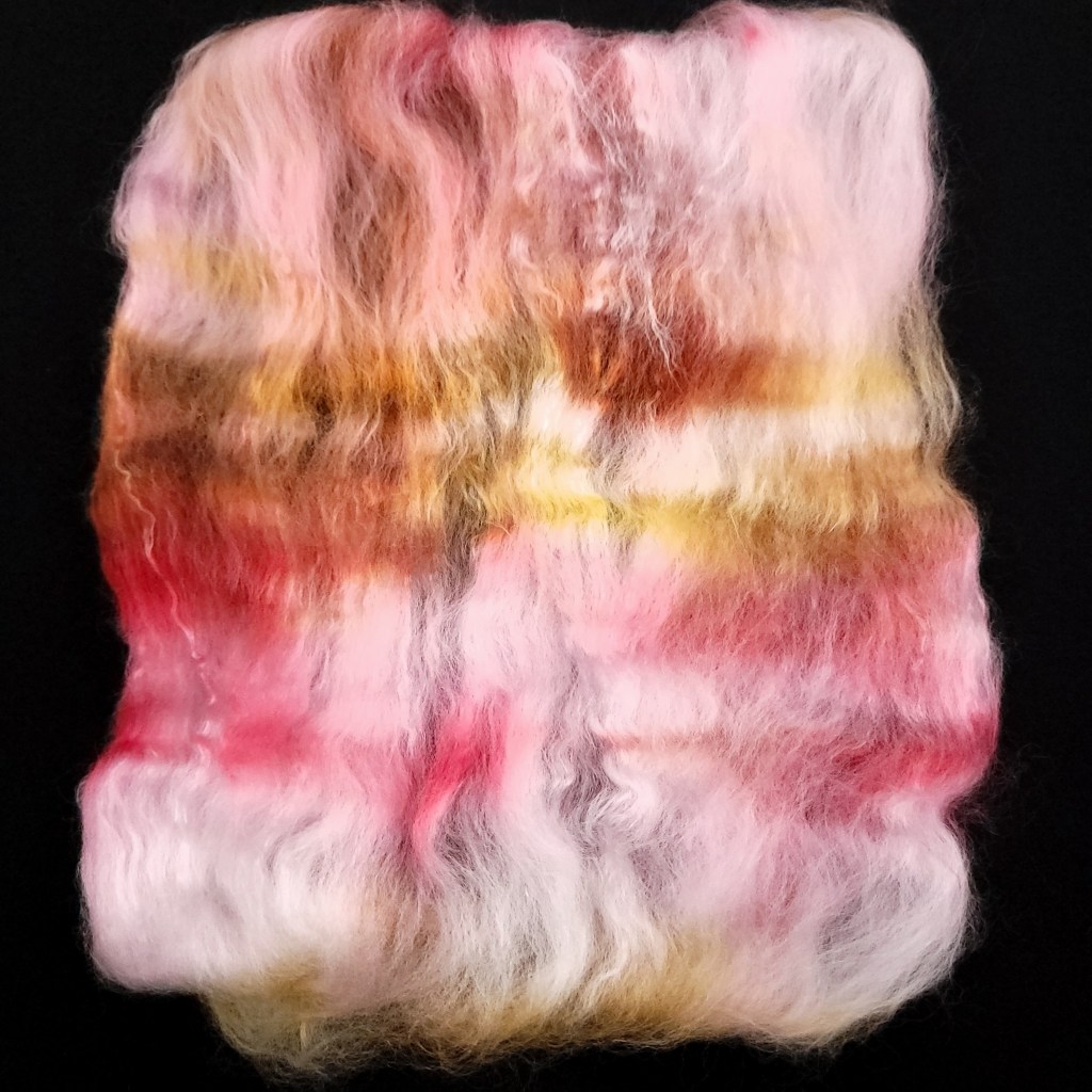A chunk of unspun fiber is spread out against a black background. While the fiber was categorized as "Medium Pink" the actual colors include pink, white, orange and gold.