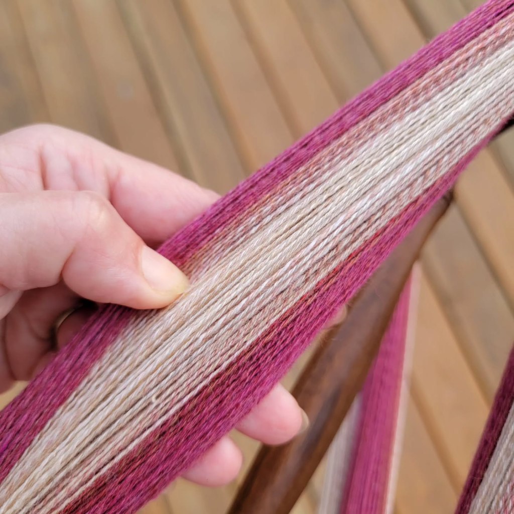 A hand holds a section of yarn spread out to show the colors and fineness of the spinning. 