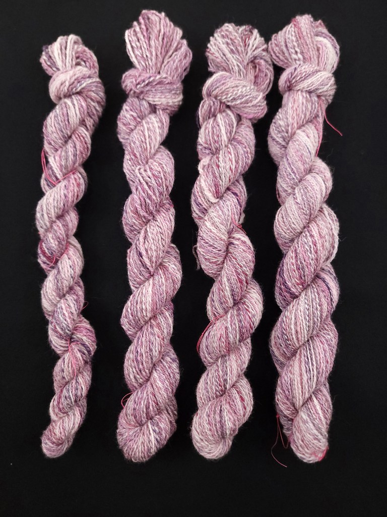 Four skeins of pink, white and purple yarn against a black background